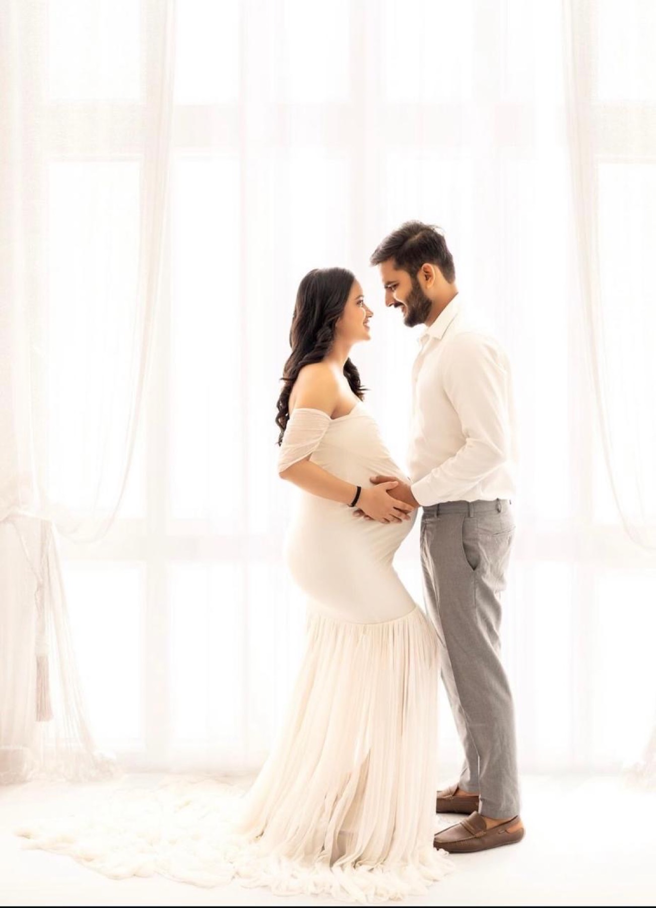 Elegant maternity couple window photoshoot in white gown